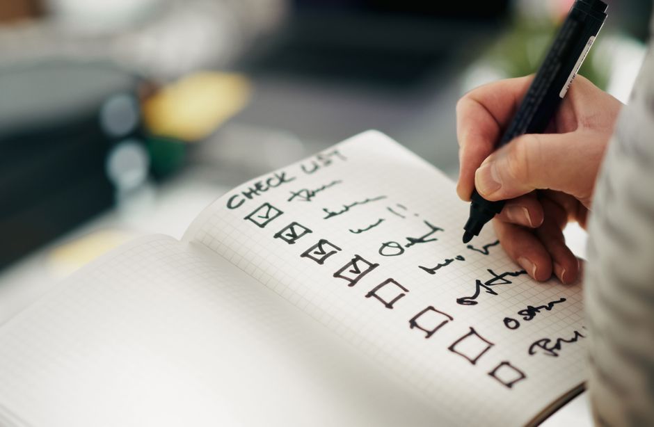 Hand writing tasks on a checklist, emphasizing productivity and organization.